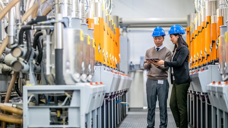 Two engineers using digital tablet while examining manufacturing machinery in factory