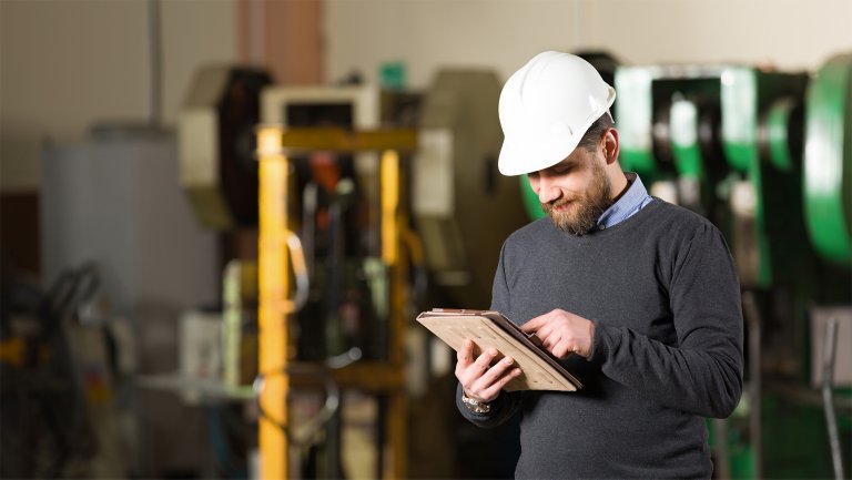 Man holding tablet device and looking at equipment on production floor