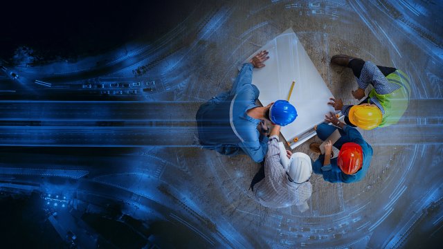Vue de dessus de quatre ingénieurs industriels portant des casques, en discussion autour de plans visant à sécuriser l’infrastructure critique face aux cybermenaces
