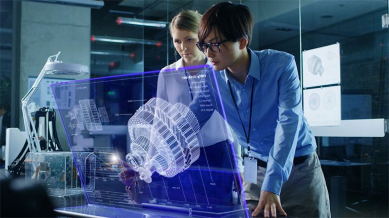 Two female employees in an office viewing information on a computer that has been projected as a larger, semi-transparent image in front of the monitor.